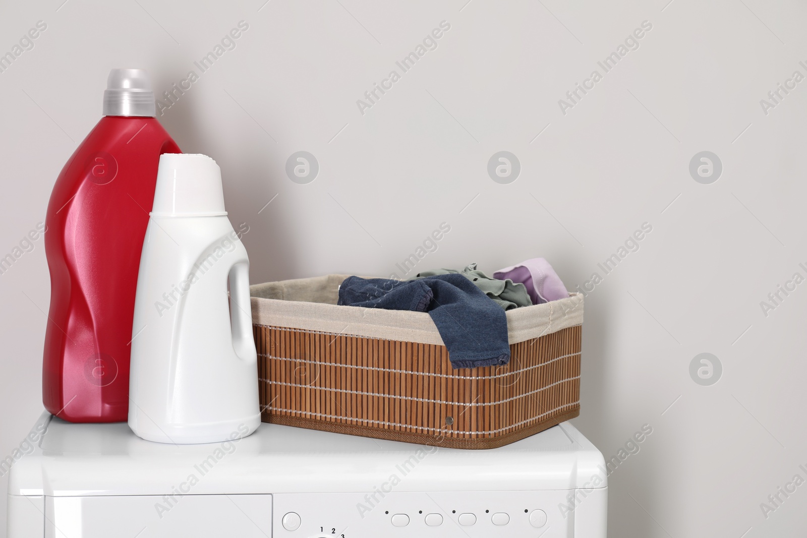 Photo of Baby clothes in wicker basket and laundry detergents on washing machine near light wall, space for text