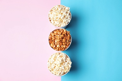 Different kinds of popcorn in paper cups on color background, top view