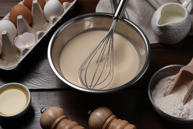 Photo of Dough, metal whisk in bowl and ingredients on wooden table