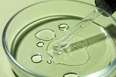 Photo of Petri dish with pipette and sample on light green background, closeup