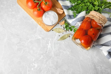 Flat lay composition with pickled tomatoes in glass jar on grey table, space for text