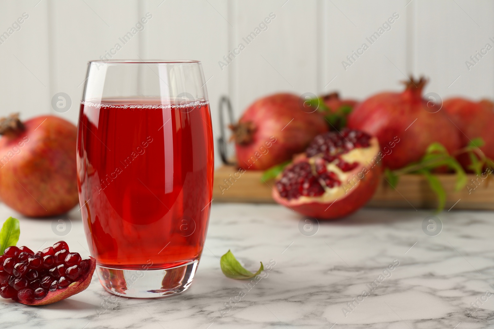 Photo of Tasty pomegranate juice in glass and fresh fruits on white marble table. Space for text