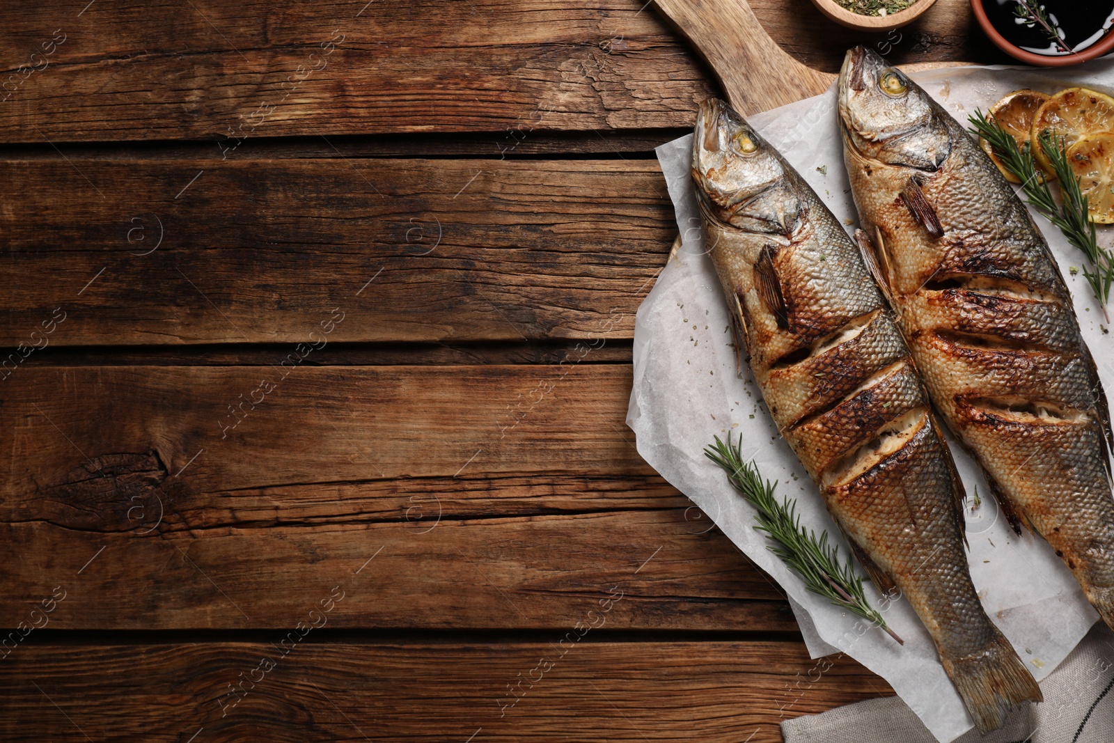 Photo of Delicious baked sea bass fish and ingredients on wooden table, flat lay. Space for text
