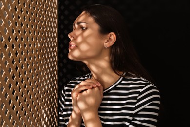 Photo of Woman listening to priest during confession near wooden partition in booth