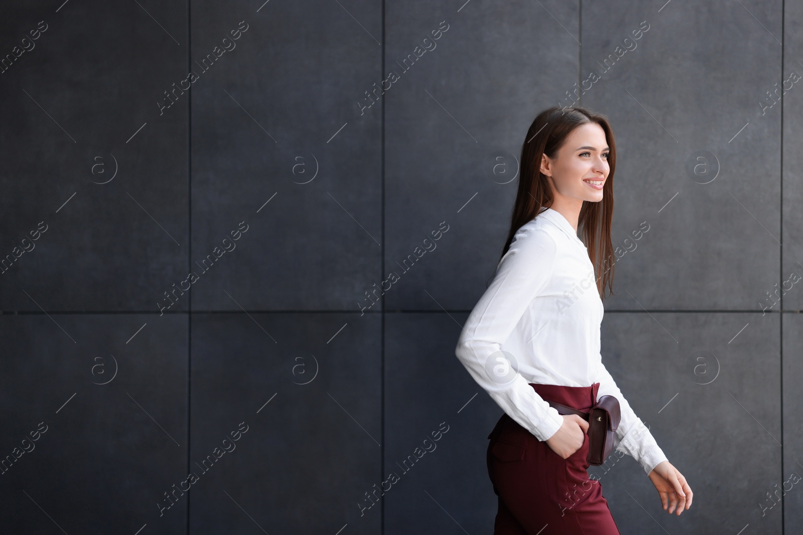 Photo of Young woman in formal clothes walking near grey wall outdoors, space for text