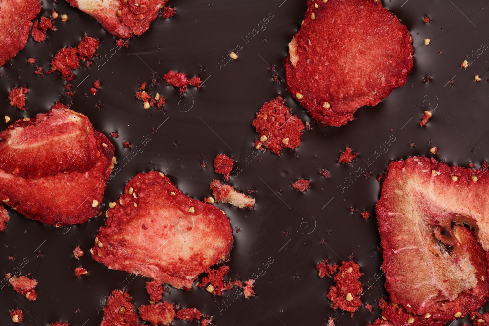 Photo of Chocolate bar with freeze dried strawberries as background, closeup