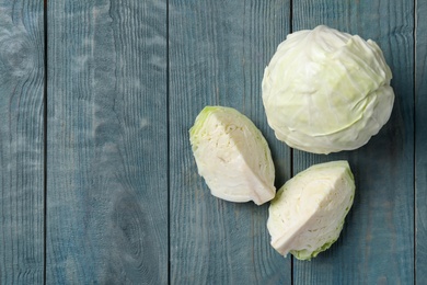 Photo of Fresh whole and cut cabbages on blue wooden table, flat lay. Space for text