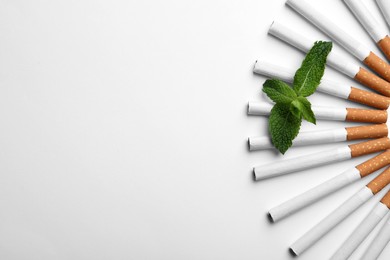 Menthol cigarettes and fresh mint leaves on white background, flat lay. Space for text