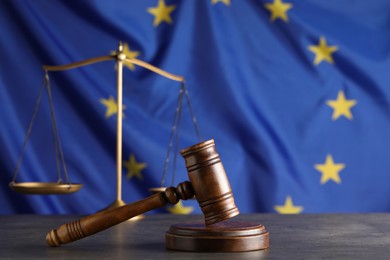 Photo of Wooden judge's gavel and Scales of justice on grey table against European Union flag