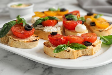 Plate of delicious tomato bruschettas on white marble table, closeup