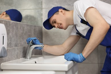 Smiling plumber wearing gloves examining faucet in bathroom