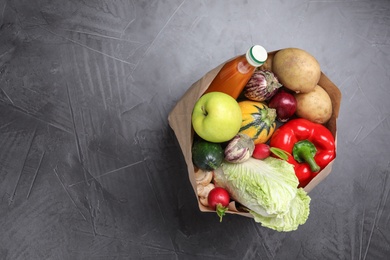 Paper package with fresh vegetables, apple and bottle of juice on dark background, top view. Space for text
