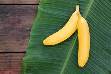 Delicious bananas and green leaf on wooden table, top view