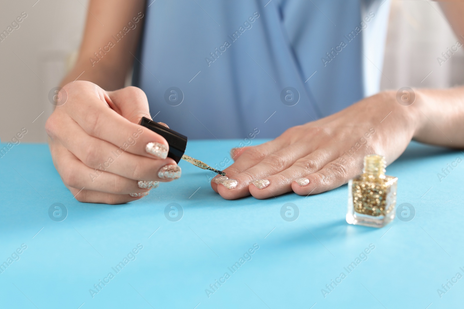 Photo of Woman applying nail polish at table, closeup. At-home manicure