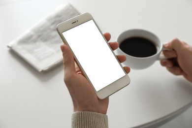 Man holding mobile phone with empty screen at table, closeup