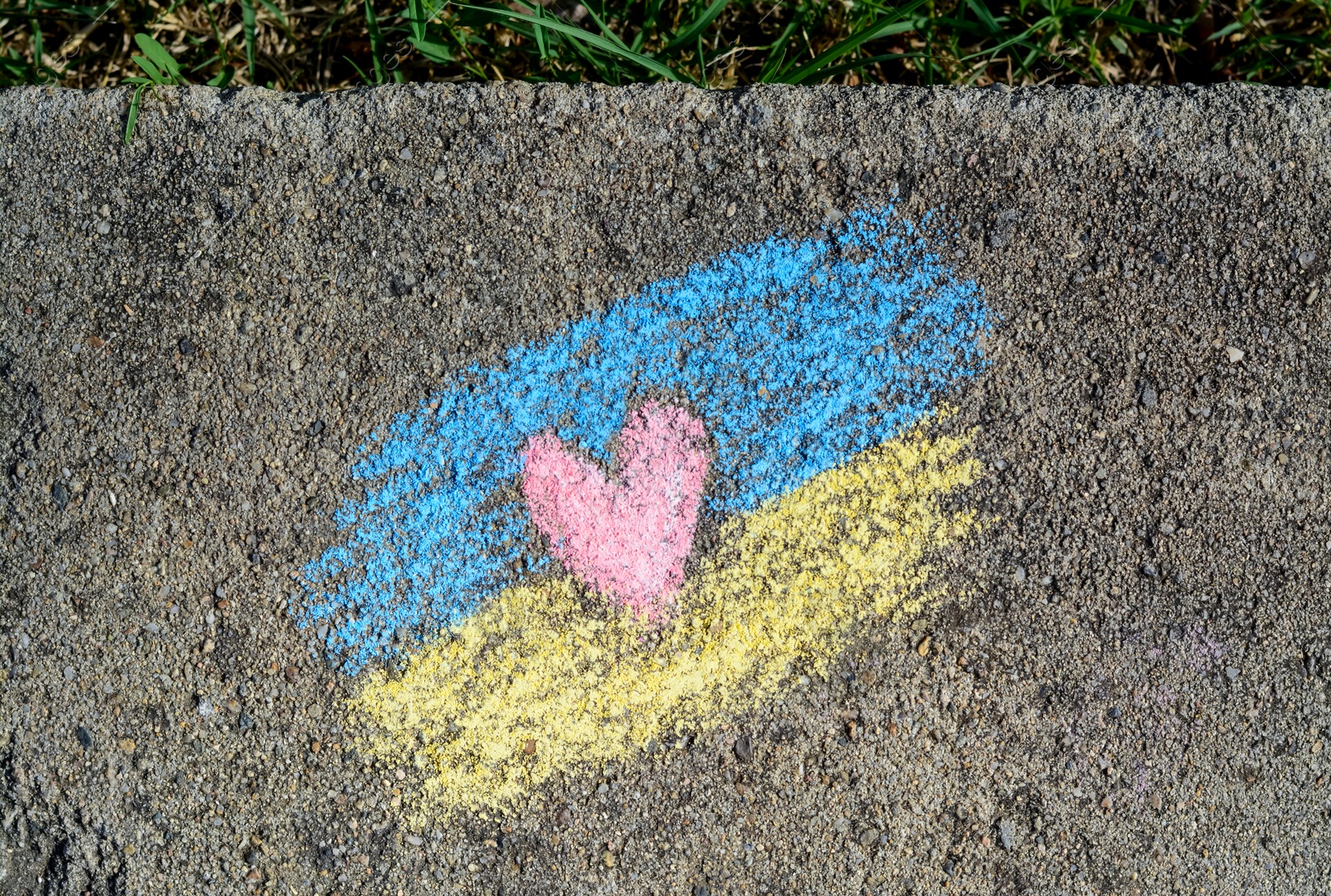 Photo of National flag of Ukraine with heart drawn by color chalk on asphalt, top view