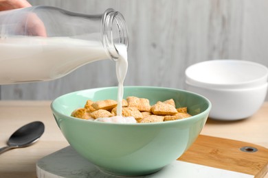 Photo of Pouring milk into bowl of tasty corn pads served for breakfast on table