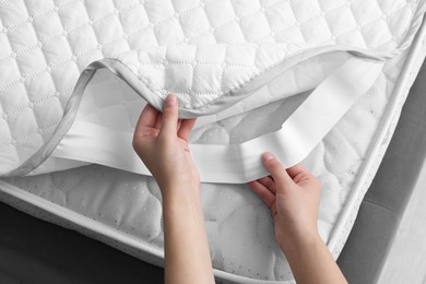 Photo of Woman putting protector on mattress, top view