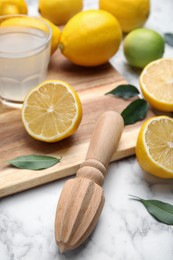 Photo of Wooden citrus reamer, fresh lemons and lime on white marble table