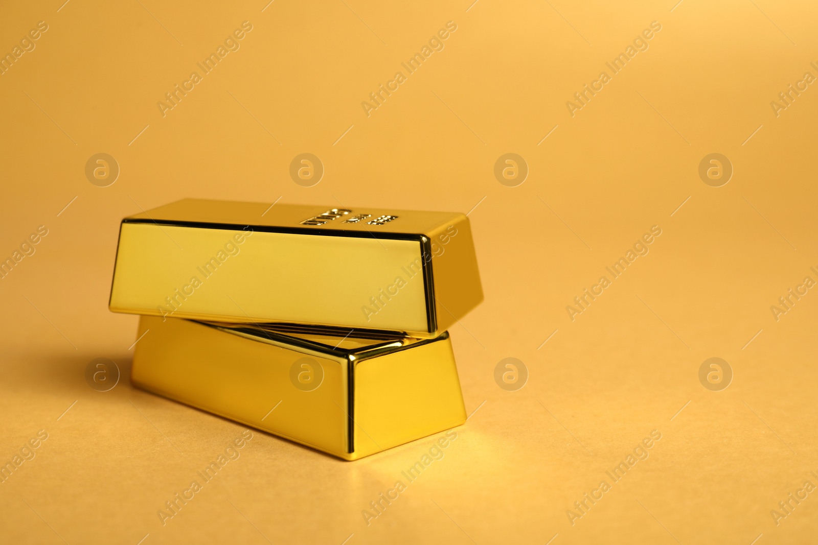 Photo of Shiny gold bars on pale orange background, closeup. Space for text