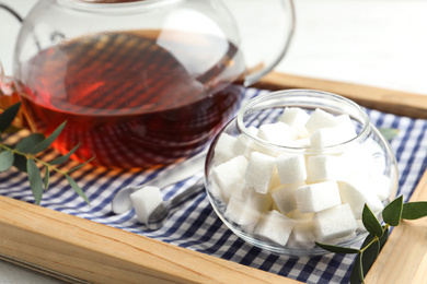 Photo of Refined sugar cubes in glass bowl and tongs on wooden tray