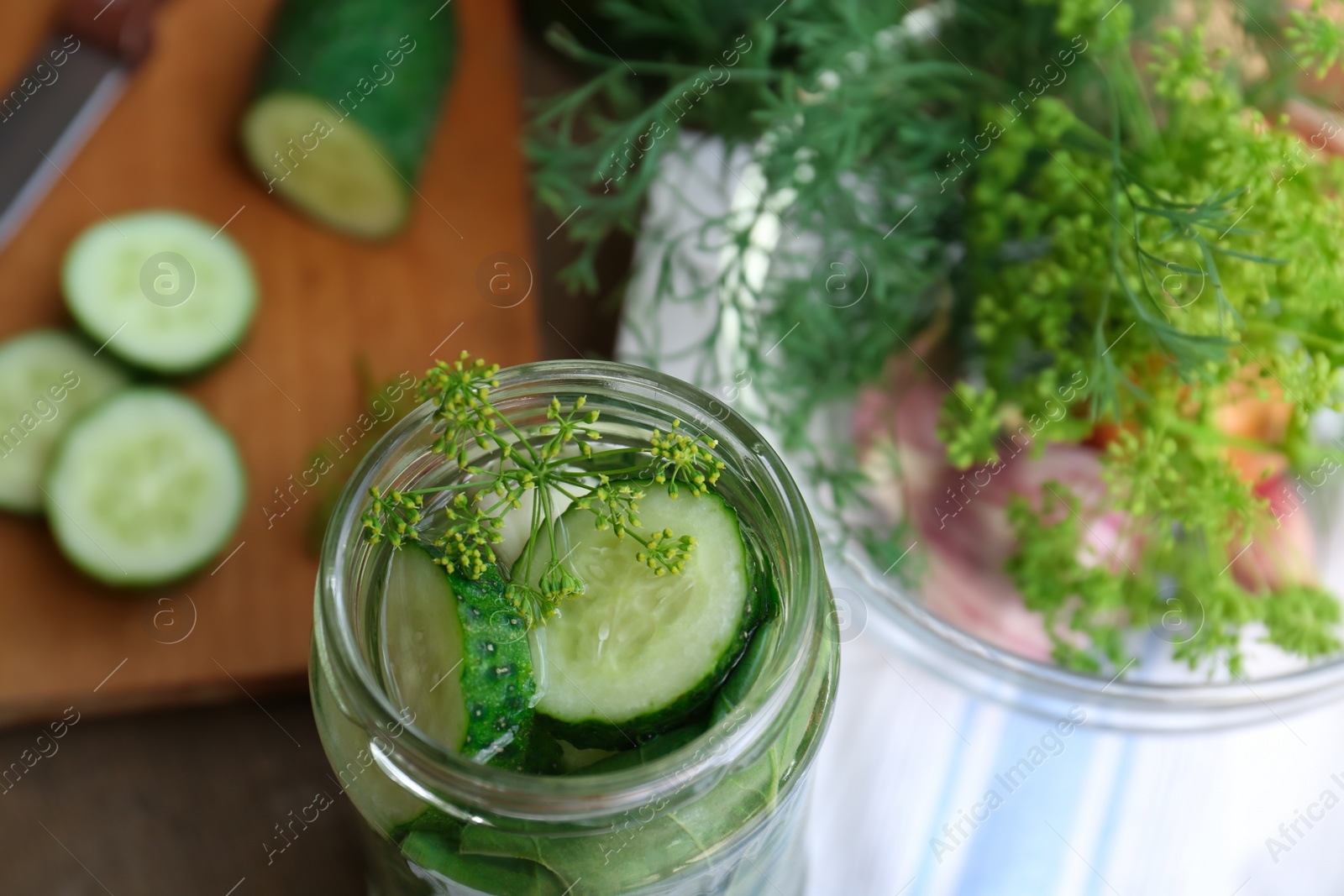 Photo of Glass jar with cucumber slices, dill and brine on table, closeup. Pickling recipe