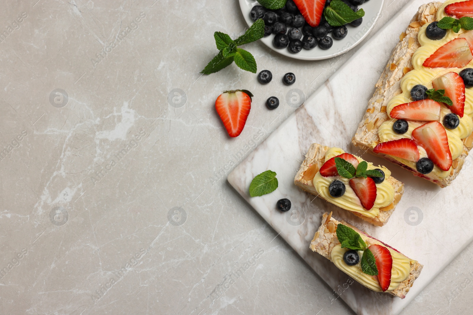 Photo of Tasty meringue roll with cream, strawberry, blueberry and mint on light grey marble table, flat lay. Space for text