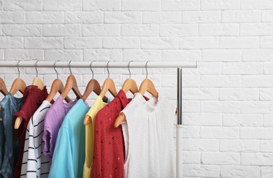 Wardrobe rack with stylish clothes near brick wall indoors. Space for text
