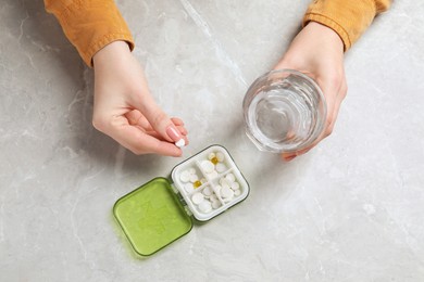 Woman holding glass of water and pill at grey marble table, top view