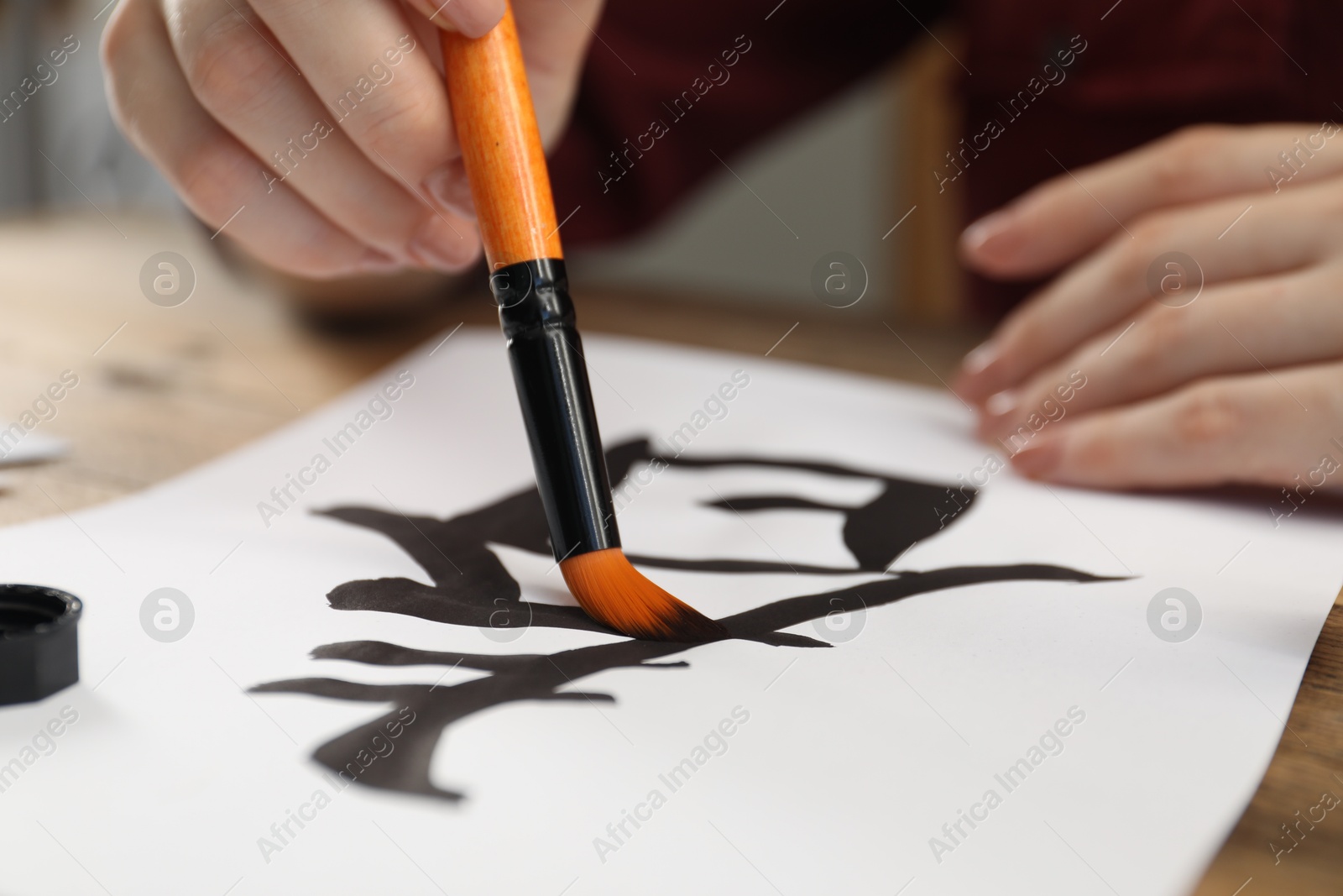 Photo of Calligraphy. Woman with brush writing hieroglyphs on paper at table, closeup