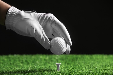 Photo of Player putting golf ball on tee against black background, closeup