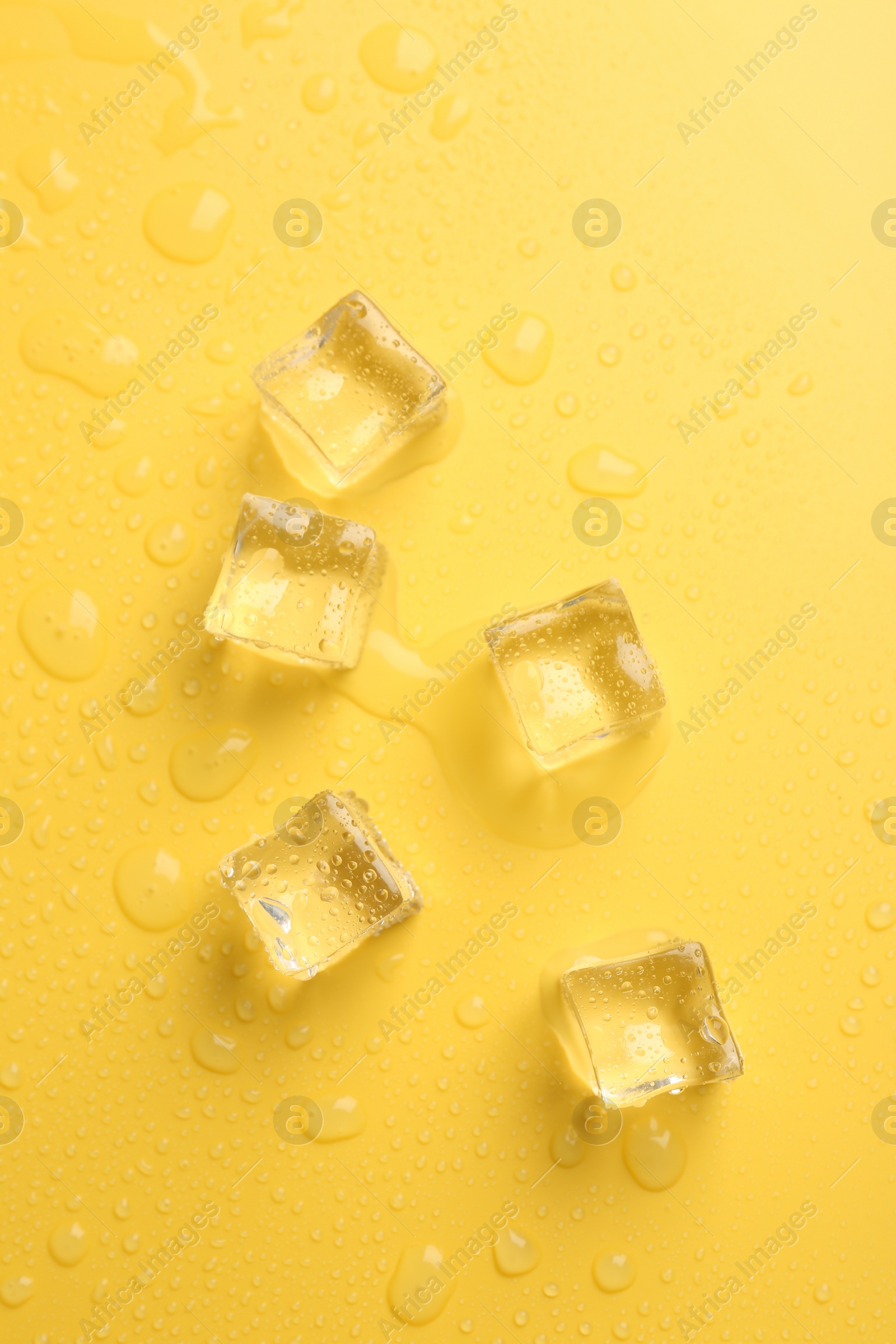 Photo of Crystal clear ice cubes on yellow background, flat lay