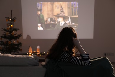 Photo of Lviv, Ukraine – January 24, 2023: Woman watching Harry Potter And The Philosopher’s Stone movie via video projector at home, back view