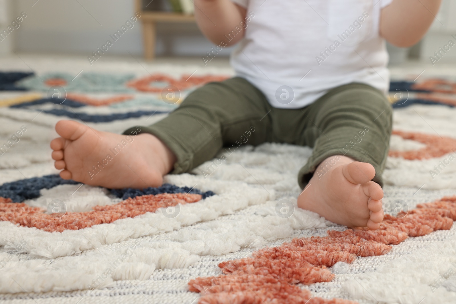 Photo of Baby sitting on soft carpet indoors, closeup