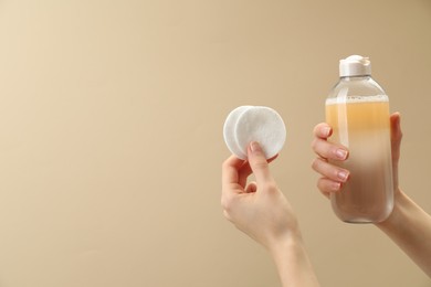 Woman holding makeup remover and cotton pads on beige background, closeup. Space for text