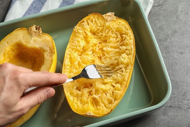 Photo of Woman scraping flesh of cooked spaghetti squash with fork on table, top view