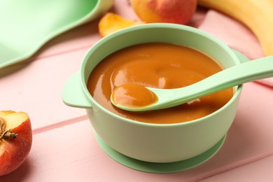 Bowl and spoon with tasty pureed baby food on pink wooden table, closeup