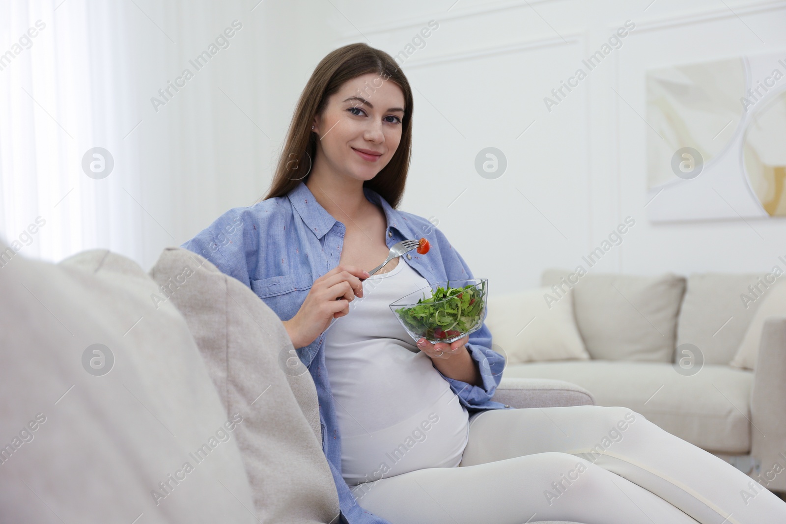 Photo of Pregnant woman with salad on sofa at home. Healthy diet
