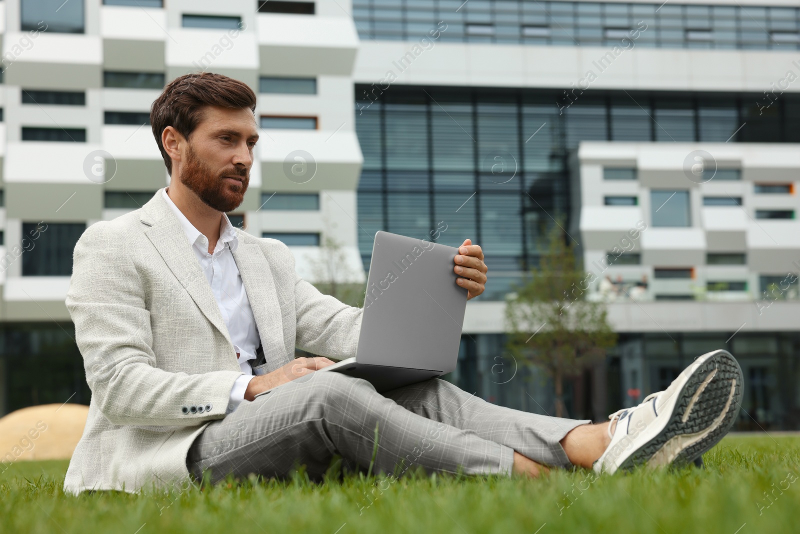 Photo of Handsome businessman with laptop on green grass outdoors