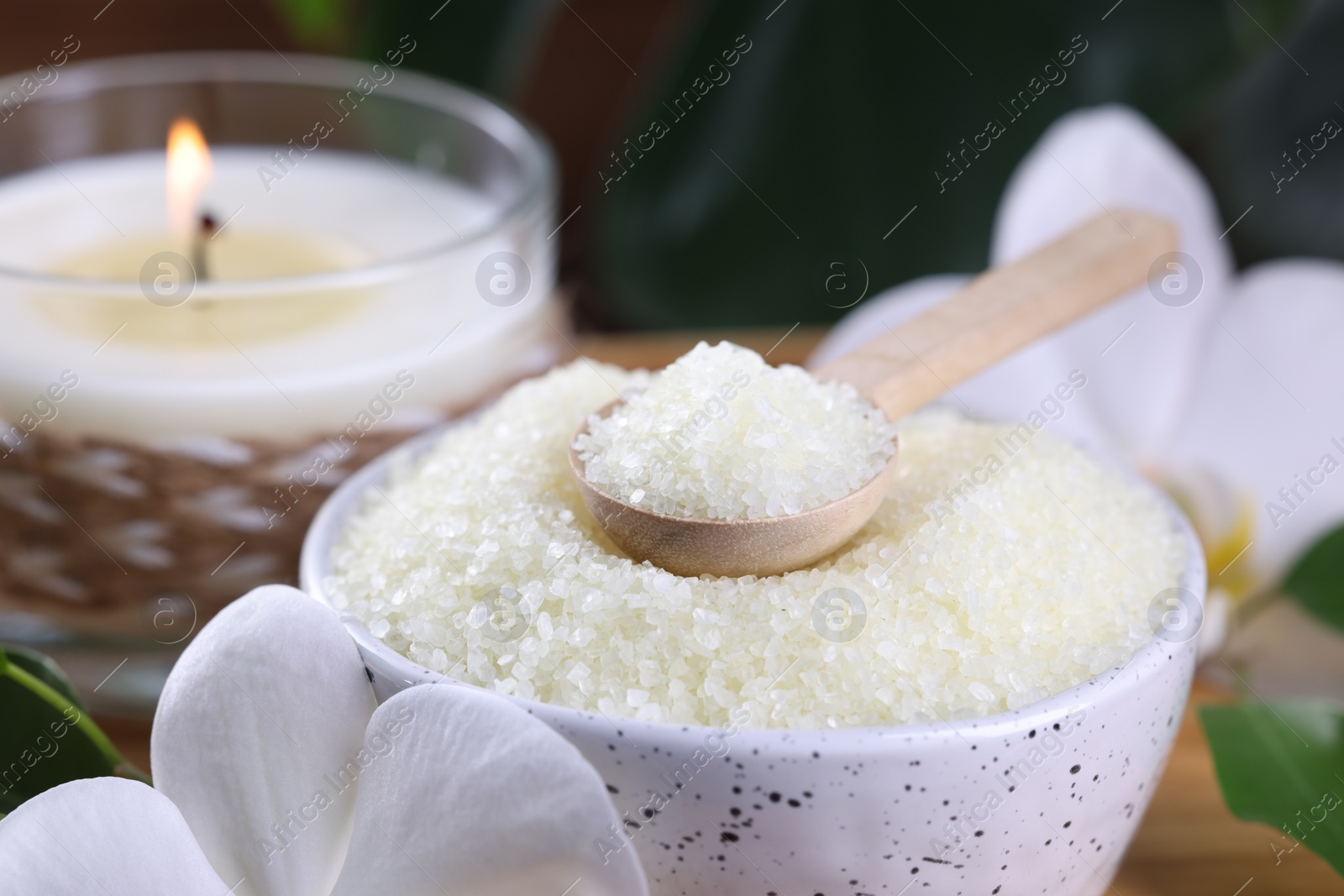 Photo of Natural sea salt in bowl, candle and beautiful orchid flower on table, closeup