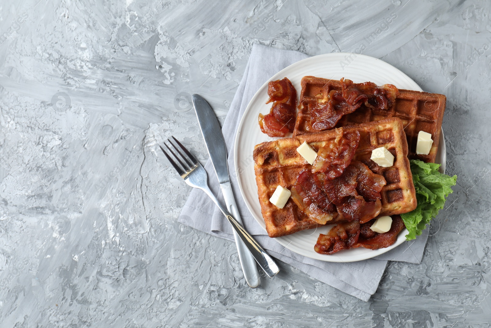 Photo of Delicious Belgium waffles served with fried bacon and butter on grey table, top view. Space for text