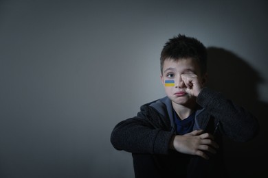 Sad little boy with picture of Ukrainian flag on cheek near light wall, space for text. Stop war in Ukraine