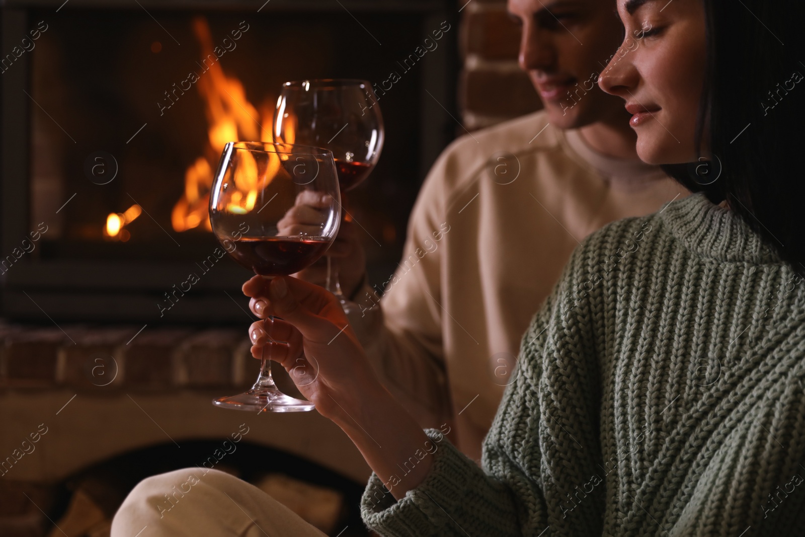 Photo of Lovely couple with glasses of wine near fireplace indoors. Winter vacation