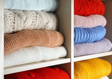 Folded colorful winter sweaters on shelves as background