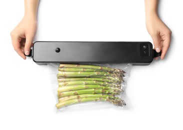 Photo of Woman using for vacuum packing with plastic bag of asparagus on white background, top view