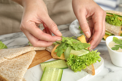 Photo of Woman making tasty sandwich at white marble table, closeup