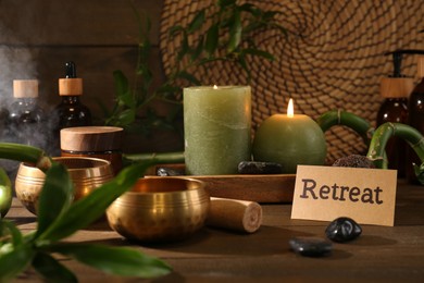 Photo of Card with word Retreat, singing bowls and burning candles on wooden table