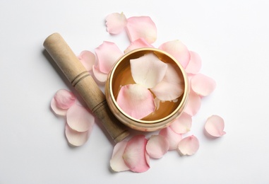 Photo of Golden singing bowl with petals and mallet on white background, flat lay. Sound healing