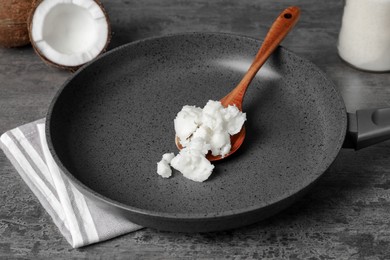 Photo of Frying pan with coconut oil and wooden spoon on grey table