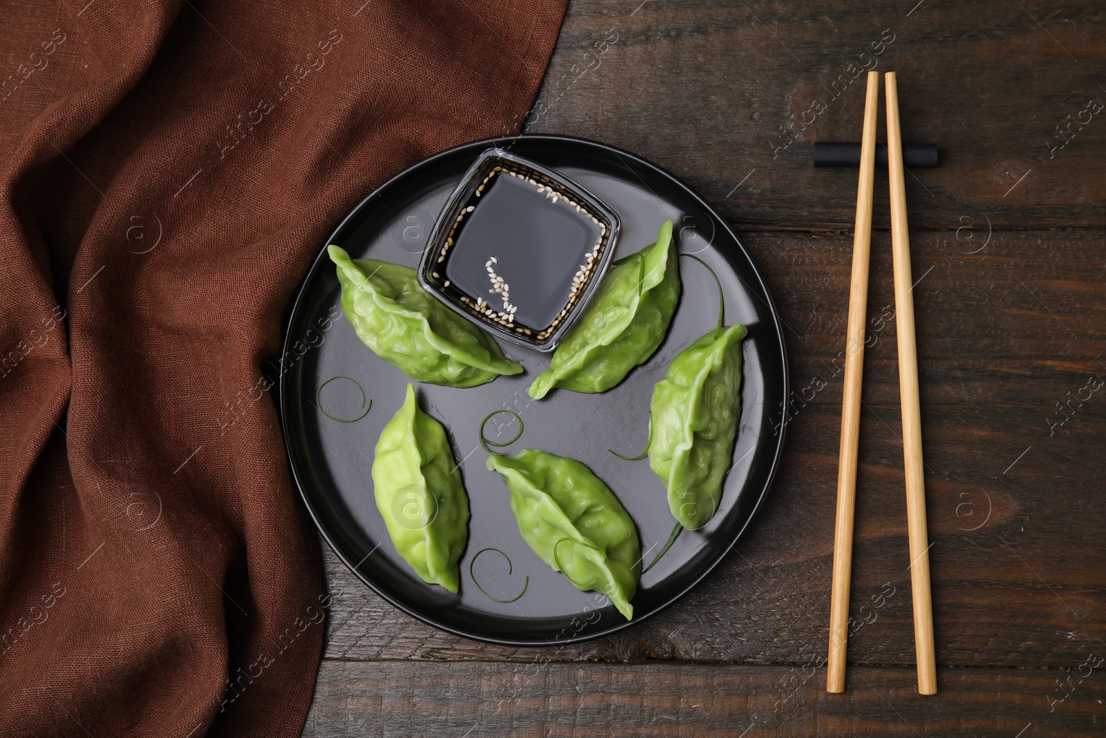 Photo of Delicious green dumplings (gyozas) with soy sauce served on wooden table, flat lay